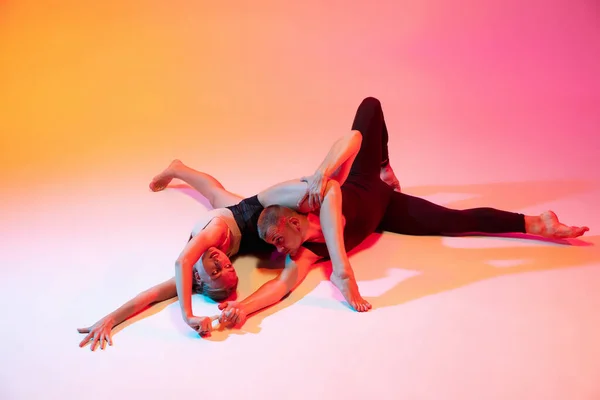 Twee dansers, stijlvol sportief koppel, mannelijke en vrouwelijke modellen dansen hedendaagse dans op kleurrijke gradiënt geel roze achtergrond in neon licht. — Stockfoto