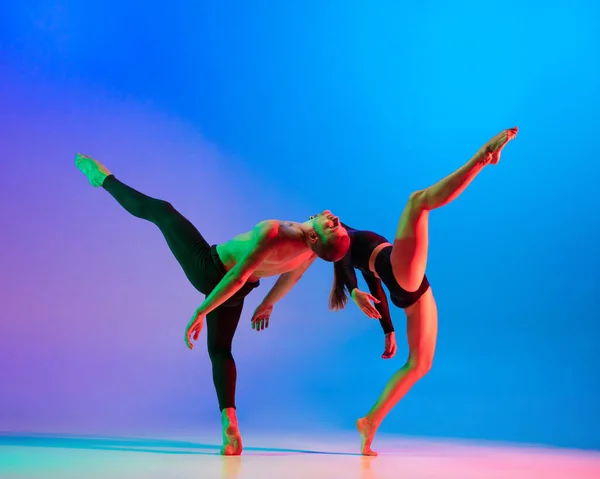 Élégant couple caucasien sportif, danseur masculin et féminin dansant la danse contemporaine sur fond rose bleu dégradé coloré au néon. — Photo