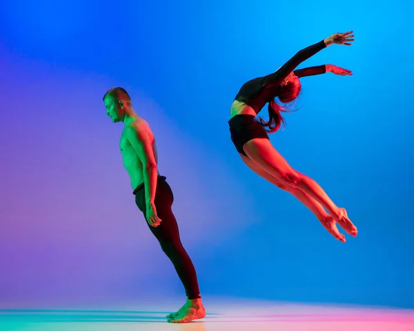 Stijlvol sportief Kaukasisch paar, mannelijke en vrouwelijke danser dansen hedendaagse dans op kleurrijke gradiënt blauw roze achtergrond in neon licht. — Stockfoto