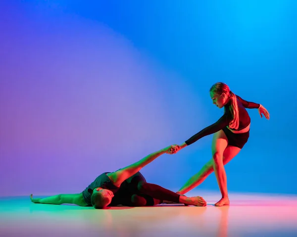 Stylowa sportowa para kaukaska, tancerka męska i żeńska tańcząca taniec współczesny na kolorowym gradientowym niebieskim różowym tle w neonowym świetle. — Zdjęcie stockowe