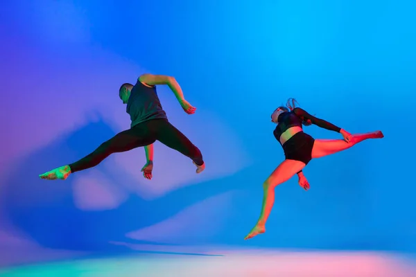 Pasangan Kaukasia yang sportif, penari laki-laki dan perempuan menari tarian kontemporer di atas warna-warni latar merah muda biru kemerahan dalam cahaya neon. — Stok Foto