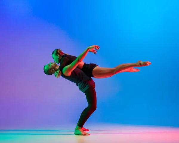 Stijlvol sportief Kaukasisch paar, mannelijke en vrouwelijke danser dansen hedendaagse dans op kleurrijke gradiënt blauw roze achtergrond in neon licht. — Stockfoto