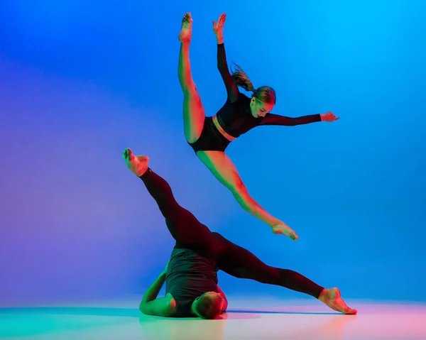 Стильная спортивная кавказская пара, мужчина и женщина танцуют современный танец на ярком голубом фоне в неоновом свете. — стоковое фото