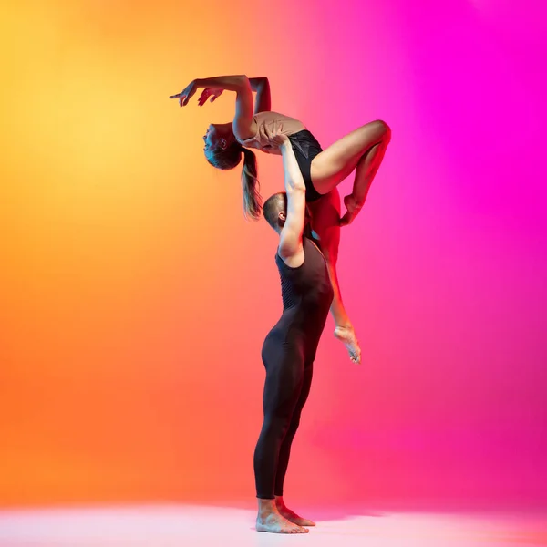 Kunstperformance. Zwei Tänzer, stilvolles sportliches Paar, männliche und weibliche Models tanzen zeitgenössischen Tanz auf farbenfrohem Gradienten gelb-rosa Hintergrund in Neonlicht. — Stockfoto