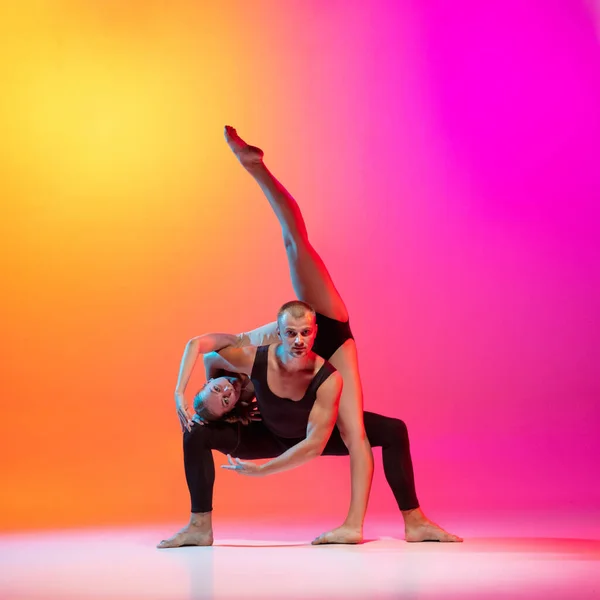 Kunstvoorstelling. Twee dansers, stijlvol sportief koppel, mannelijke en vrouwelijke modellen dansen hedendaagse dans op kleurrijke gradiënt geel roze achtergrond in neon licht. — Stockfoto