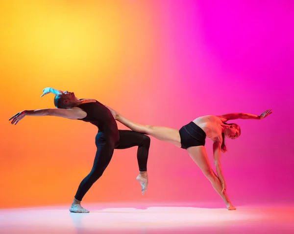 Искусство. Два танцора, стильная спортивная пара, мужские и женские модели танцуют современный танец на ярко-желтом розовом фоне в неоновом свете. — стоковое фото