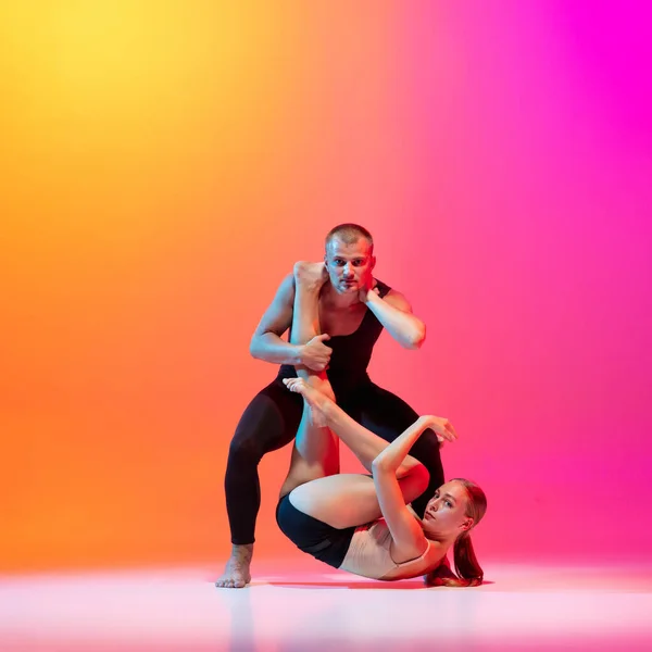 Kunstvoorstelling. Twee dansers, stijlvol sportief koppel, mannelijke en vrouwelijke modellen dansen hedendaagse dans op kleurrijke gradiënt geel roze achtergrond in neon licht. — Stockfoto