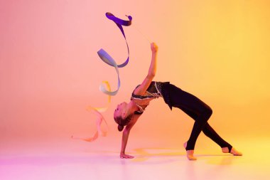 Küçük bir kızın portresi, ritmik jimnastik sanatçısı, neon rengi pembe sarı stüdyo arka planında izole edilmiş. Spor, eylem, arzu, eğitim, aktif yaşam tarzı kavramı