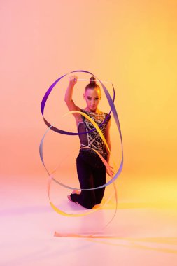 Küçük bir kızın portresi, ritmik jimnastik sanatçısı, neon rengi pembe sarı stüdyo arka planında izole edilmiş. Spor, eylem, arzu, eğitim, aktif yaşam tarzı kavramı
