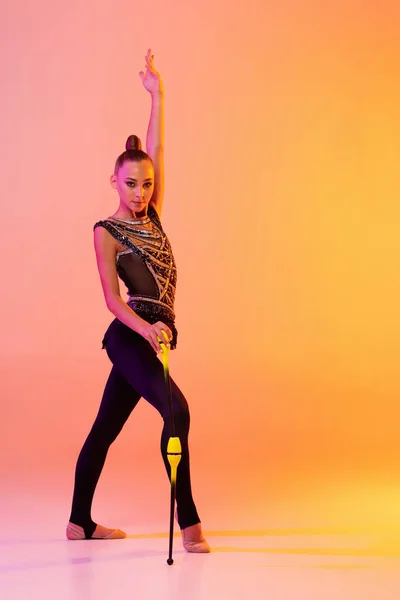 Una chica joven, artista de gimnasia rítmica en traje de escenario, disfraz deportivo aislado en fondo de estudio amarillo rosado en neón. Concepto de deporte — Foto de Stock