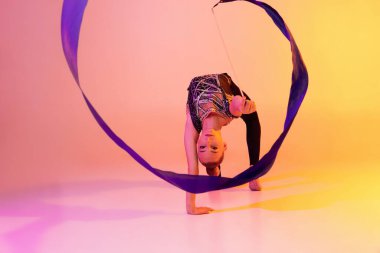 Küçük bir kızın portresi, ritmik jimnastik sanatçısı, neon rengi pembe sarı stüdyo arka planında izole edilmiş. Spor, eylem, arzu, eğitim, aktif yaşam tarzı kavramı