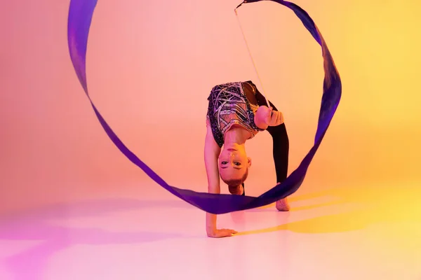 Portret van klein meisje, ritmische gymnastiek kunstenaar geïsoleerd op roze gele studio achtergrond in neon. Begrip sport, actie, aspiratie, onderwijs, actieve levensstijl — Stockfoto