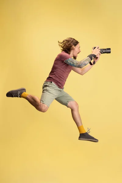 Retrato de joven, fotógrafo, camarógrafo con cámara aislada sobre fondo de estudio amarillo. Concepto de ocupación, trabajo, emociones divertidas meme — Foto de Stock