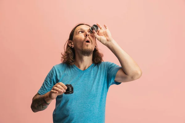 Porträt eines jungen Mannes, Fotografen, Kameramanns mit Kameraobjektiv, der isoliert auf rosa Studiohintergrund Spaß hat. Begriffe wie Beruf, Job, lustige Meme — Stockfoto