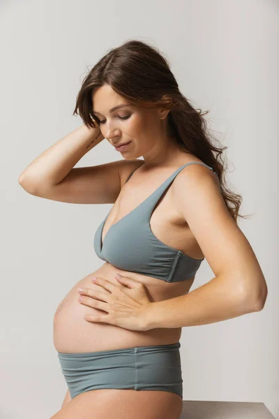 Tiempo feliz, esperando. Retrato de una hermosa mujer embarazada sonriente en lencería aislada sobre fondo gris de estudio. Belleza natural, maternidad feliz, concepto de feminidad. —  Fotos de Stock