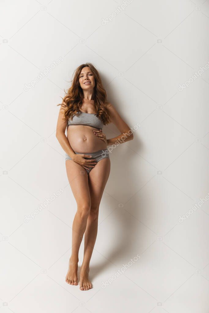Portrait of sensual pregnant woman in lingerie isolated over grey studio background. Natural beauty, happy motherhood, femininity concept.