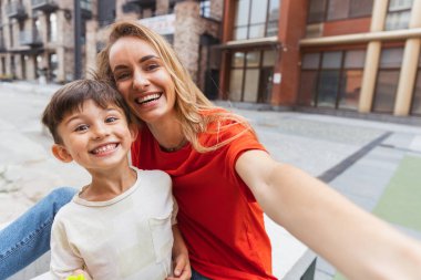 İki kişi, anne ve küçük tatlı oğlu sokakta dolaşıyorlar, yazın ticaret meydanında, açık havada. Aile zamanı, birliktelik, ebeveynlik ve mutlu çocukluk kavramı..