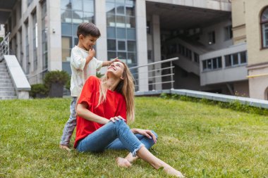 Mutlu bir anne ve küçük sevimli bir oğul yazın açık havada, halka açık bir parkta geziniyor. Aile zamanı, birliktelik, ebeveynlik ve mutlu çocukluk kavramı..