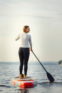 Genç beyaz kadın, sporcu, raket tahtasında duran turist, SUP, yalnız çalışıyor. Aktif yaşam, spor, boş zaman aktivite konsepti
