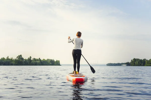 Ung vit kvinna, idrottsman, turist stående på paddelbräda, SUP, öva ensam. Aktivt liv, idrott, fritidsaktiviteter — Stockfoto