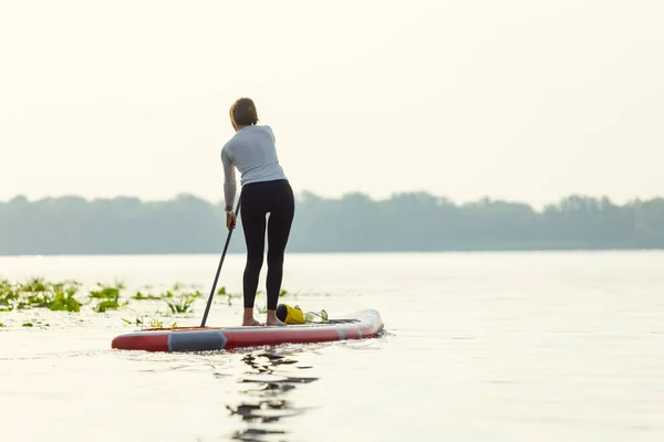 Junge Kaukasierin, Sportlerin, Touristin, die auf einem Paddelbrett steht, SUP macht, allein übt. Aktives Leben, Sport, Freizeitkonzept — Stockfoto