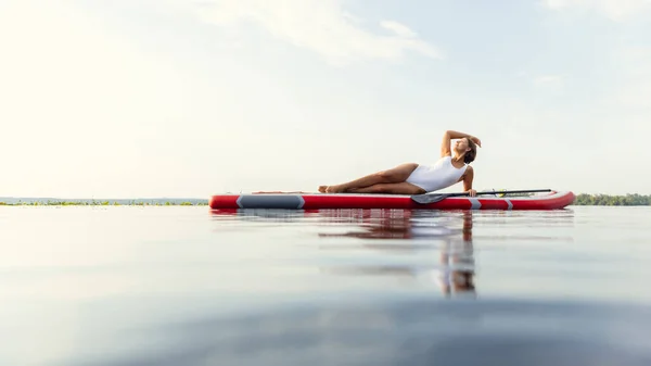 One young Caucasian beautiful slim girl sunbathe on summer evening on river on paddle board, SUP alone. Active life, sport, leisure activity concept — Stock Photo, Image