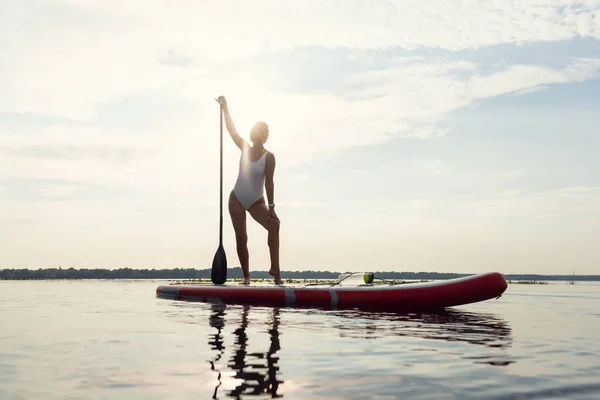 One young Caucasian beautiful slim girl sunbathe on summer evening on river on paddle board, SUP alone. Active life, sport, leisure activity concept — Stock Photo, Image