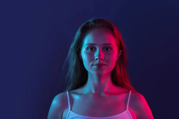 Retrato de una joven hermosa niña aislada sobre fondo de estudio azul oscuro en luz de neón rosa. Concepto de emociones humanas, expresión facial, juventud, ventas, anuncio. — Foto de Stock