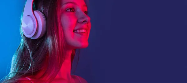 Портрет молодой улыбающейся девушки, изолированной на темно-синем фоне студии в розовом неоновом свете. Человеческие эмоции, выражение лица, молодость, продажи, реклама. — стоковое фото
