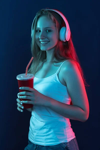 Portrait de jeune fille souriante isolée sur fond studio bleu foncé dans la lumière rose néon. Concept d'émotions humaines, expression faciale, jeunesse, vente, publicité. — Photo