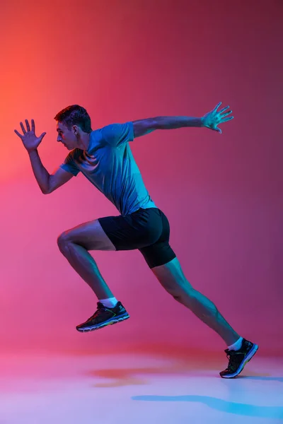 Portrét bělošského profesionálního sportovce, trénink běžců izolovaný na růžovém pozadí studia s modrým neonovým filtrem, světlo. Svalnatý, sportovní muž. — Stock fotografie