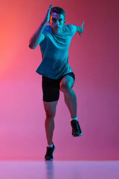 Portrat of Caucasian professional male athlete, runner training isolated on pink studio background with blue neon filter, light. Muscular, sportive man. — Stock Photo, Image