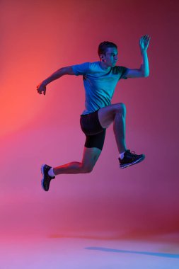 Portrat of Caucasian professional male athlete, runner training isolated on pink studio background with blue neon filter, light. Muscular, sportive man. clipart