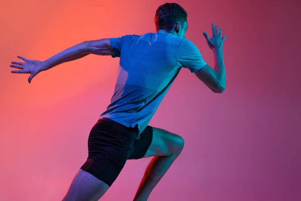 Portrat av kaukasiska professionell manlig idrottsman, löpare utbildning isolerad på rosa studio bakgrund med blå neon filter, ljus. Muskulös, sportig man. Bakifrån — Stockfoto