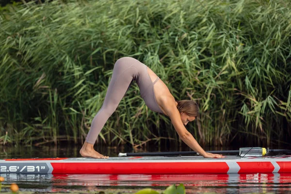 Une jeune caucasienne belle fille mince faisant du yoga, pilates sur planche à pagaie, SUP seul le matin d'été. Vie active, sport, loisir concept d'activité — Photo