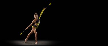 Küçük bir kızla el ilanı, parlak sahne kostümlü ritmik jimnastik sanatçısı karanlık stüdyo arka planında ışık altında izole edilmiş. Spor, eylem, arzu, aktif yaşam tarzı kavramı