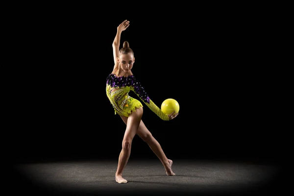 Ritratto di bambina, ginnastica ritmica in costume da palcoscenico luminoso isolata su sfondo scuro da studio in raggio di luce. Il concetto di sport, azione, aspirazione, stile di vita attivo — Foto Stock