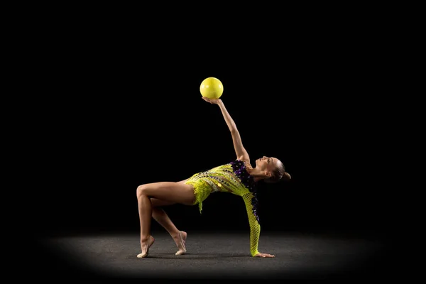 Retrato de niña, artista de gimnasia rítmica en traje de escenario brillante aislado en el fondo oscuro del estudio en rayo de luz. Concepto de deporte, acción, aspiración, estilo de vida activo — Foto de Stock