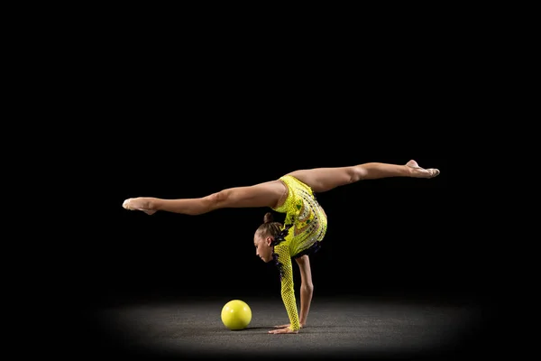 Szczupła sportowa dziewczyna, artystka gimnastyki rytmicznej w jasnym stroju sceny odizolowana na ciemnym tle studio w promieniach światła. Pojęcie sportu, działania, aspiracji, aktywnego stylu życia — Zdjęcie stockowe