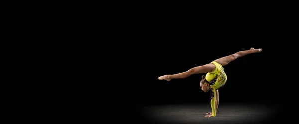 Chica deportiva delgada, artista de gimnasia rítmica en traje de escenario brillante aislado en fondo de estudio oscuro en rayo de luz. Concepto de deporte, acción, aspiración, estilo de vida activo — Foto de Stock