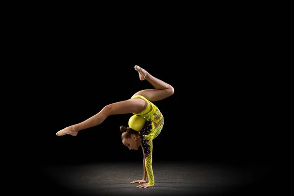 Porträtt av liten flicka, rytmisk gymnastik artist i ljusa scenkostym isolerad på mörk studio bakgrund i stråle av ljus. Begreppet idrott, handling, strävan, aktiv livsstil — Stockfoto