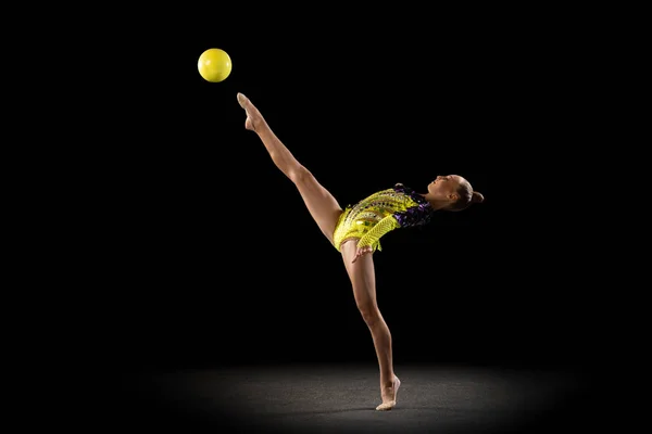 Retrato de niña, artista de gimnasia rítmica en traje de escenario brillante aislado en el fondo oscuro del estudio en rayo de luz. Concepto de deporte, acción, aspiración, estilo de vida activo — Foto de Stock