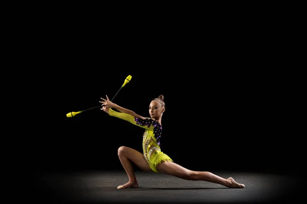 Portret van een klein meisje, ritmische gymnastiek kunstenaar in helder podium kostuum geïsoleerd op donkere studio achtergrond in een straal van licht. Concept sport, actie, ambitie, actieve levensstijl — Stockfoto