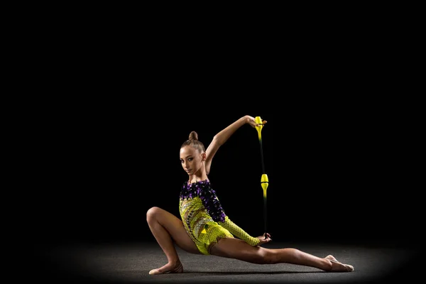 Portret van een klein meisje, ritmische gymnastiek kunstenaar in helder podium kostuum geïsoleerd op donkere studio achtergrond in een straal van licht. Concept sport, actie, ambitie, actieve levensstijl — Stockfoto