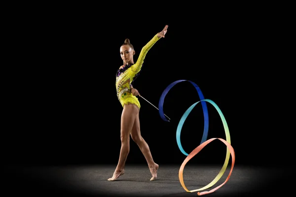 Een sportief emotioneel meisje, ritmische gymnastiek kunstenaar geïsoleerd op donkere achtergrond in een straal van licht. Concept sport, actie, ambitie, schoonheid, actieve levensstijl — Stockfoto