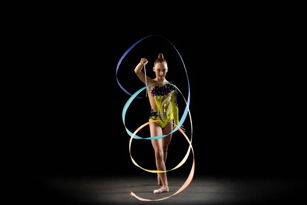 Een sportief emotioneel meisje, ritmische gymnastiek kunstenaar geïsoleerd op donkere achtergrond in een straal van licht. Concept sport, actie, ambitie, schoonheid, actieve levensstijl — Stockfoto