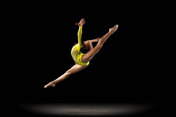 Стройная спортивная девушка, артистка художественной гимнастики в ярком сценическом костюме, изолированная на темном студийном фоне в лучах света. Концепция спорта, действия, стремления, активного образа жизни — стоковое фото