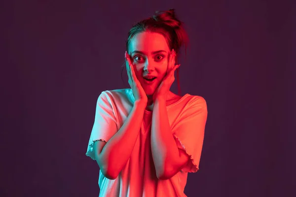 Potret gadis cantik dengan pakaian kasual terisolasi di latar belakang studio ungu gelap dengan lampu neon merah, filter. Konsep emosi manusia, ekspresi wajah. — Stok Foto
