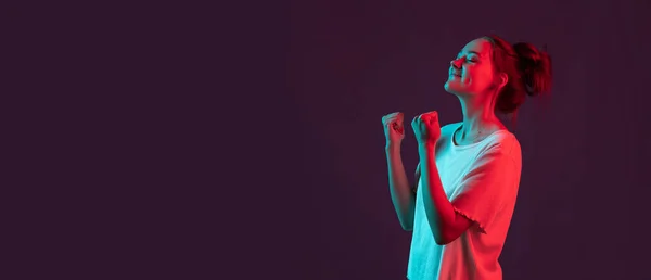Retrato de una hermosa joven aislada sobre fondo de estudio púrpura oscuro en luz de neón rojo, filtro. Concepto de emociones humanas, expresión facial. —  Fotos de Stock