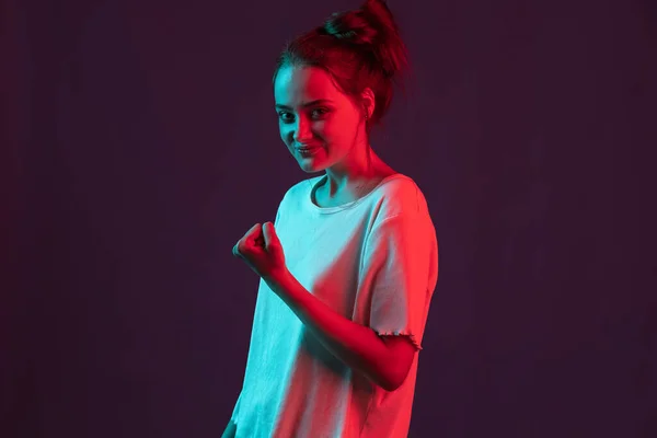 Retrato de doce, menina bonita isolado no fundo do estúdio roxo escuro em luz de néon vermelho, filtro. Conceito de emoções humanas, expressão facial. — Fotografia de Stock